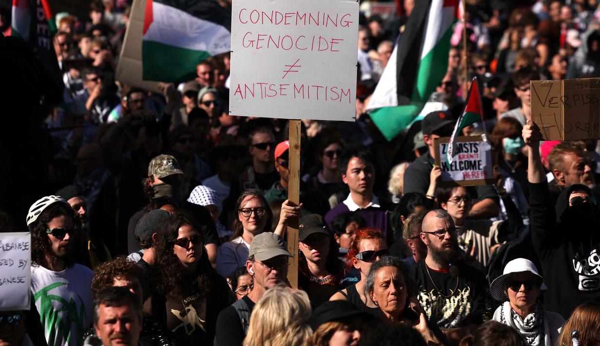Hingga kini, serangan Israel di Gaza telah menewaskan lebih dari 72.000 warga Palestina dan melukai lebih dari 171.000 lainnya, serta menghancurkan sekitar 90 persen infrastruktur di wilayah tersebut. Tampak dalam foto, para pengunjuk rasa memegang bendera dan spanduk di luar stasiun Flinders Street selama kunjungan Presiden Israel, Isaac Herzog, di Melbourne, Australia, pada Kamis 12 Februari 2026. (MARTIN KEEP/AFP)