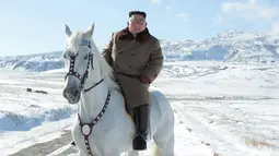Pemimpin Korea Utara Kim Jong-un tersenyum saat berada di atas kuda putih saat salju turun di gunung Paektu (16/10/2019). Kim Jong-un tampil mengenakan kaca mata dengan mantel tebal berwarna coklat.  (Photo by STR/KCNA VIA KNS/AFP)