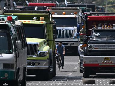 Seorang pria mengendarai sepedanya di jalan yang diblokir oleh pengemudi truk selama protes di Bogota, Kolombia, Selasa (3/9/2024). (Raul ARBOLEDA / AFP)