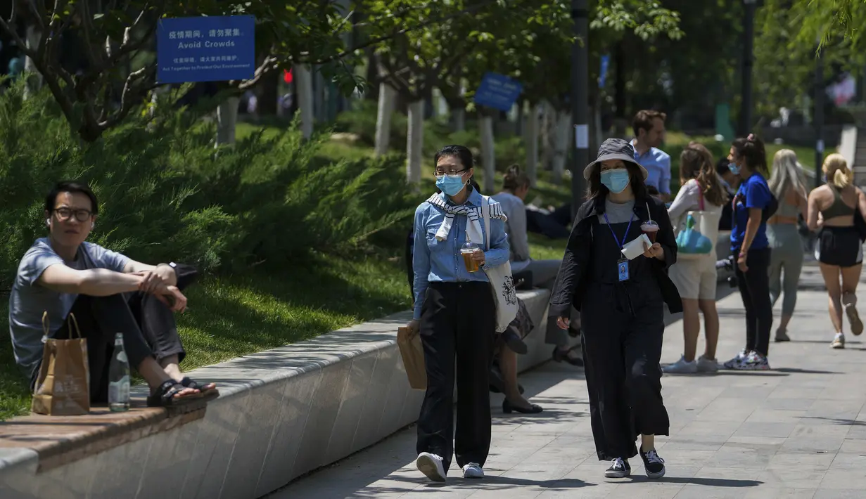 <p>Perempuan bermasker berjalan melewati orang-orang yang beristirahat di sepanjang kanal yang menampilkan pemberitahuan langkah-langkah pandemi untuk menyarankan warga agar tidak berkumpul di Beijing, China, Selasa (17/5/2022). Pada Minggu (15/5) kemarin, Beijing memperpanjang aturan untuk bekerja dari rumah di empat distrik. Itu sudah melarang layanan makan di restoran dan membatasi transportasi umum, di antara langkah-langkah lainnya. (AP Photo/Andy Wong)</p>