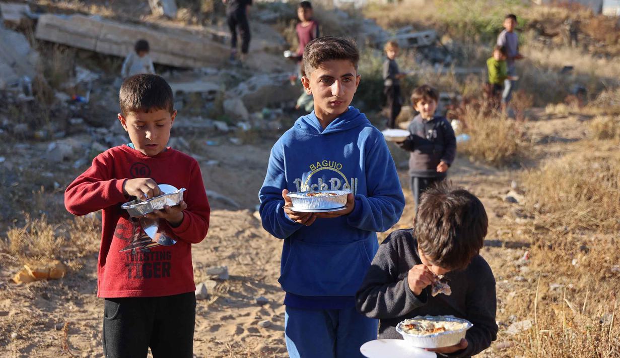 Saat ini, setidaknya ada 640.700 jiwa atau sekitar 32 persen dari populasi Gaza menghadapi kondisi darurat pangan. Tampak dalam foto, anak-anak pengungsi membawa paket makanan yang dibagikan oleh kakak beradik Palestina, Lina Zeid dan Aya Zeid, sebagai bagian dari kegiatan amal di daerah Al-Tuam, sebelah barat Jabalia, Jalur Gaza Utara pada Rabu 6 Mei 2026. (Omar AL-QATTAA/AFP)