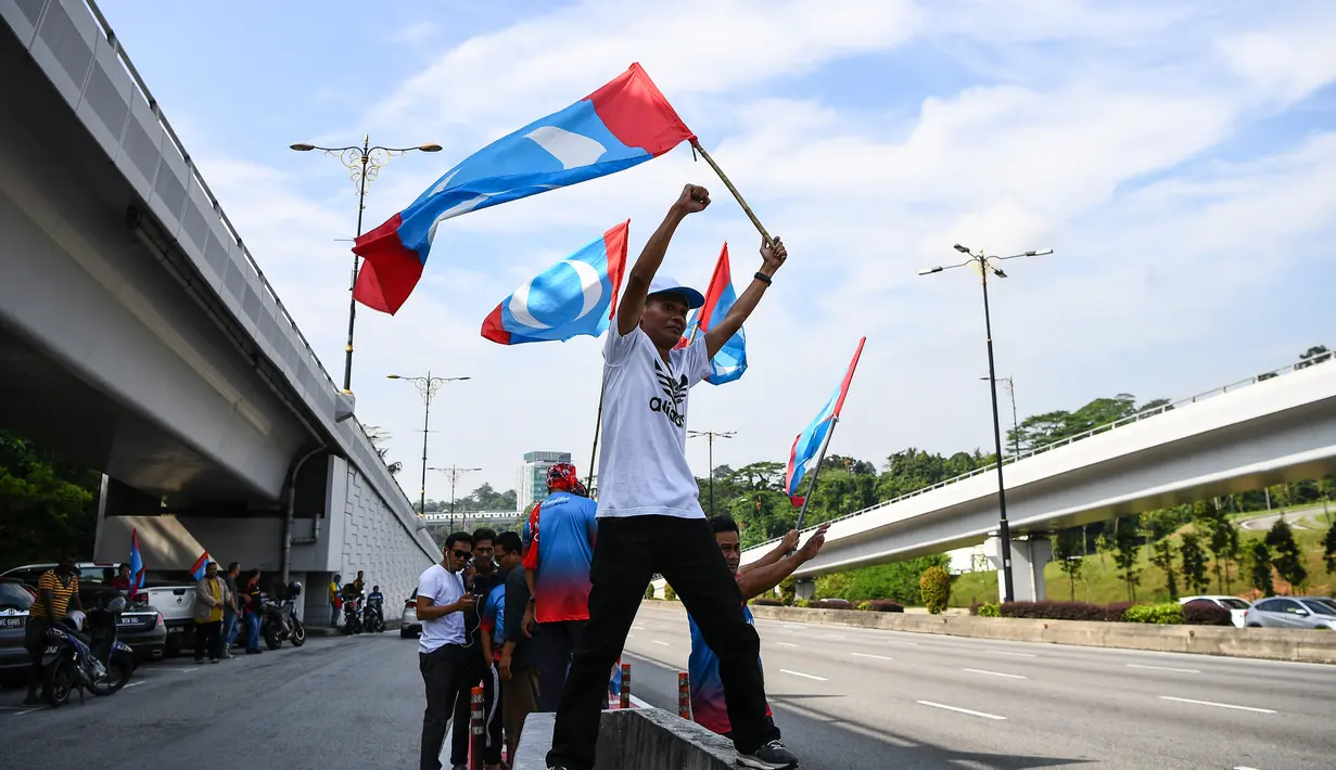 Warga melambaikan bendera Pakatan Harapan di sepanjang jalan menuju Istana Negara menjelang pelantikan Mahathir Mohamad sebagai PM Malaysia di Kuala Lumpur, Kamis (10/5). Mahathir akan menjadi perdana menteri ketujuh Negeri Jiran. (AFP/Manan VATSYAYANA)