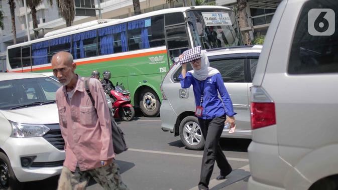 Seorang wanita menyebrang selama gelombang panas di Jakarta, Selasa (22/10/2019). BMKG memprediksi wilayah Indonesia akan mengalami panas selama kurang lebih satu minggu ini. Hal ini dikarenakan matahari yang berada dekat dengan jalur khatulistiwa. (Liputan6.com/Faizal Fanani)