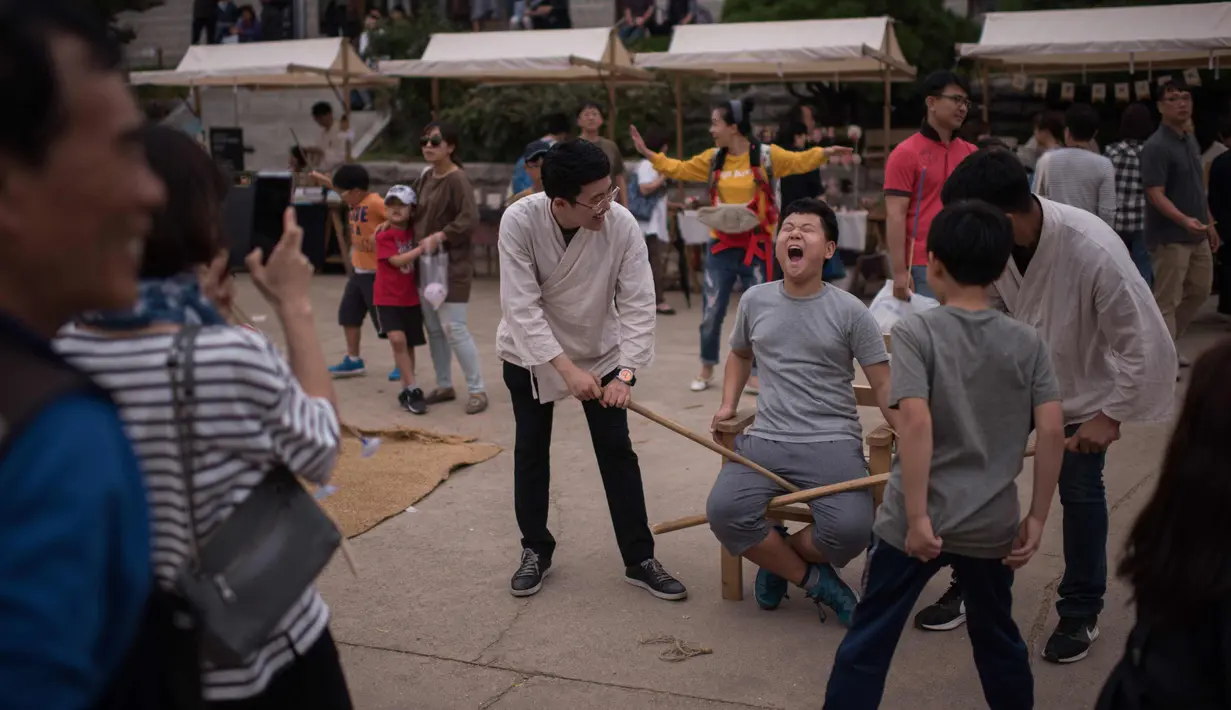 Seorang anak mengambil bagian dalam permainan yang menampilkan metode hukuman tradisional, saat perayaan Chuseok di desa hanok Namsan di Seoul (5/10). (AFP Photo/Ed Jones)