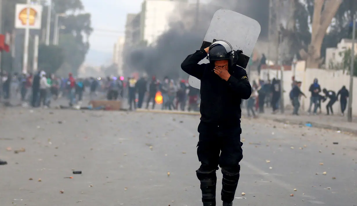 Polisi anti huru hara terkena gas air mata yang dilemparkan rekannya untuk membubarkan demonstrasi di Kasserine, Tunisia, Kamis (21/1). Para pengangguran muda menuntut solusi dari masalah pengangguran yang meliputi negaranya. (REUTERS/Amine Ben Aziza)
