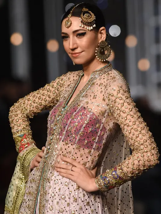 Seorang model mengenakan busana rancangan desainer Dnnus Dlrar selama Pantene Hum Bridal Couture Week di Lahore, Minggu (9/12). Kreasi gaun pengantin yang ditampilkan didominasi kain sari yang menjadi ciri khas wanita Pakistan. (ARIF ALI / AFP)
