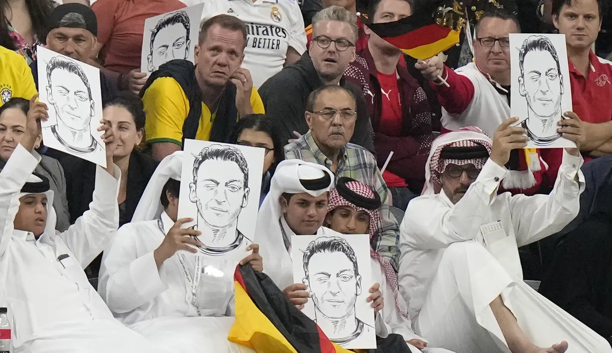 Penonton memegang foto Mesut Ozil di tribun selama pertandingan Spanyol vs Jerman pada laga Grup E Piala Dunia 2022  di Stadion Al Bayt, Senin (28/11/2022) dini hari WIB. Muncul sejumlah spekulasi bahwa aksi tersebut merupakan sindiran balik kepada Timnas Jerman yang protes atas keputusan FIFA dan Qatar yang melarang dukungan terhadap LGBT di Piala Dunia 2022. (AP Photo/Matthias Schrader)