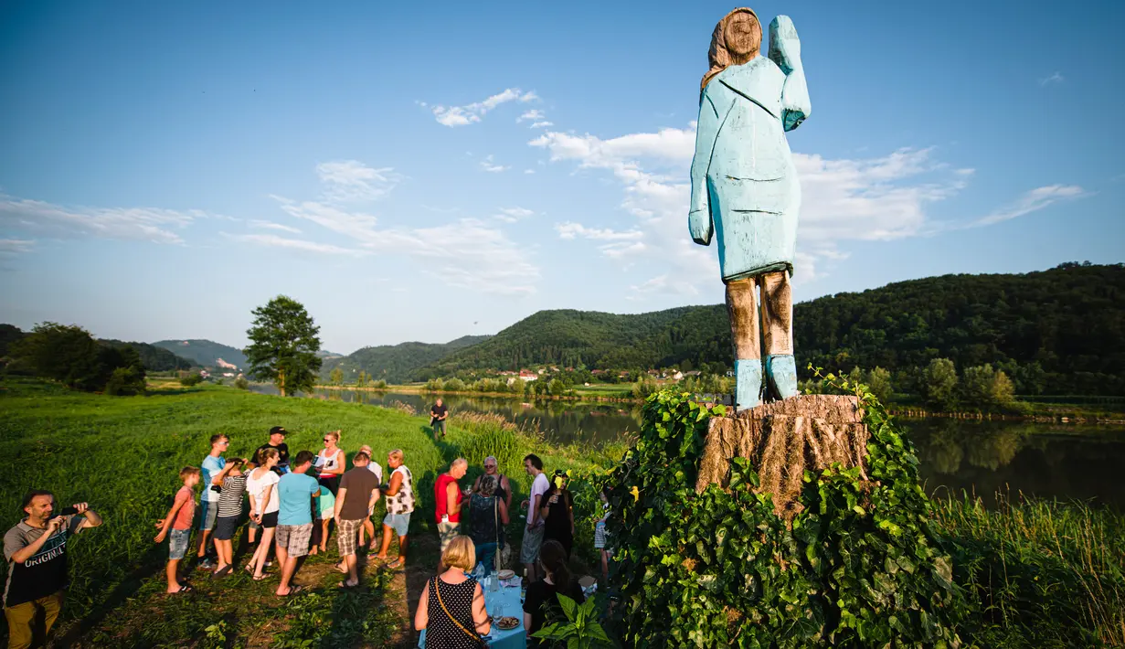 Orang-orang berkumpul dekat patung kayu yang menampilkan sosok Melania Trump di pinggiran Sevnica, Slovenia, 5 Juli 2019. Patung raksasa seukuran manusia itu  menampilkan sosok Melania yang mengenakan gaun biru yang dikenakan pada pelantikan suaminya tahun 2017. (Jure Makovec/AFP)