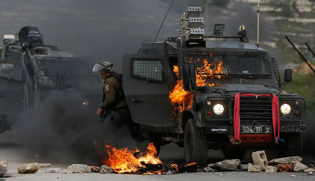 Tentara Israel meninggalkan kendaraan yang terbakar oleh lemparan bom molotov warga Palestina di pinggiran Kota Ramallah, Tepi Barat, Rabu (27/3). Bentrokan ini sebagai bentuk protes terhadap tahanan Palestina yang berada di Israel. (AP Photo/Majdi Mohammed)
