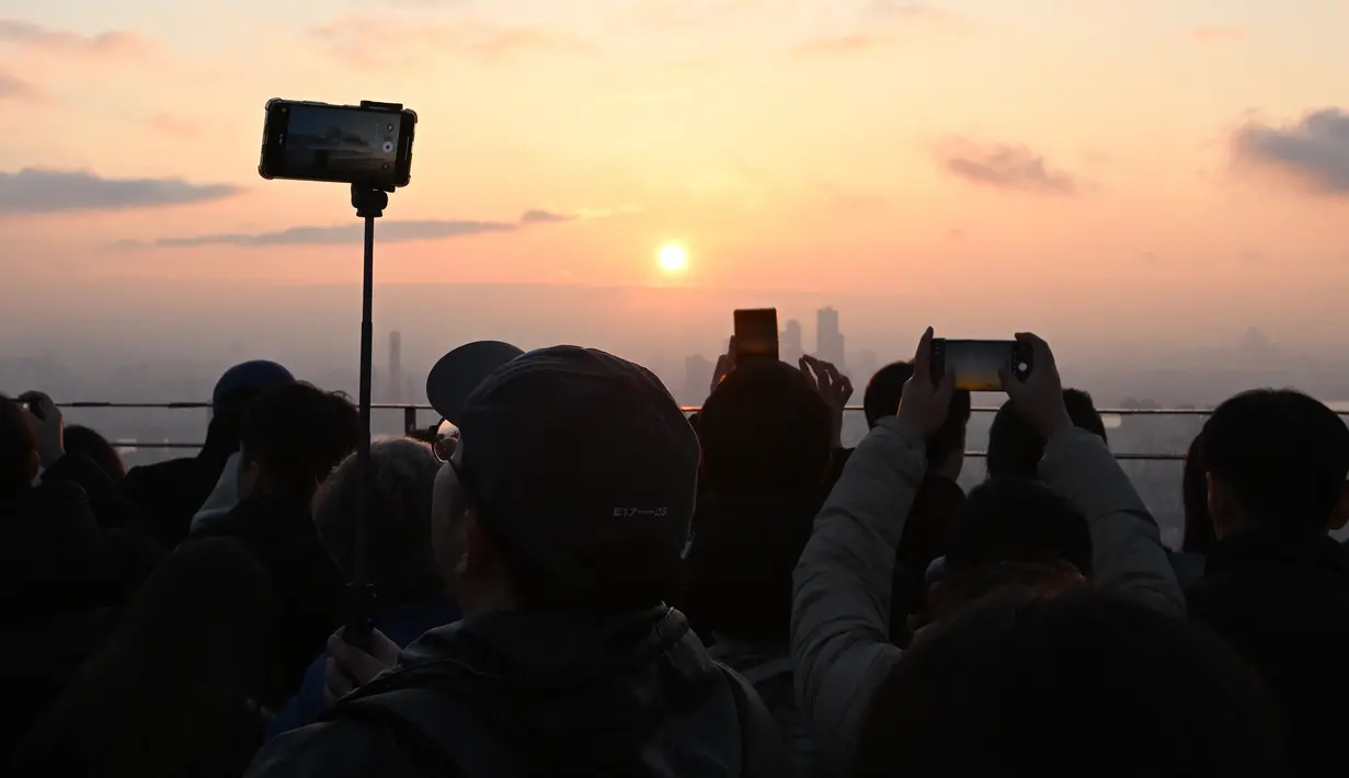 Orang-orang mengambil gambar matahari terbenam terakhir tahun ini di dek observasi menara Namsan di Seoul, Korea Selatan, Minggu (31/12/2023). (Jung Yeon-je / AFP)
