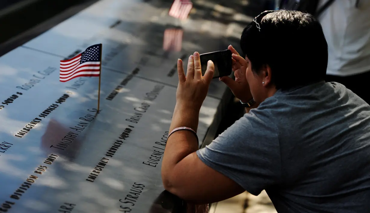 Seorang wanita memotret bendera nasional yang diletakkan di situs nama-nama para korban peristiwa serangan 11 September 2001 lalu di National September 11 Memorial and Museum at the World Trade Center, New York, Sabtu (10/9). (REUTERS/Mark Kauzlarich)