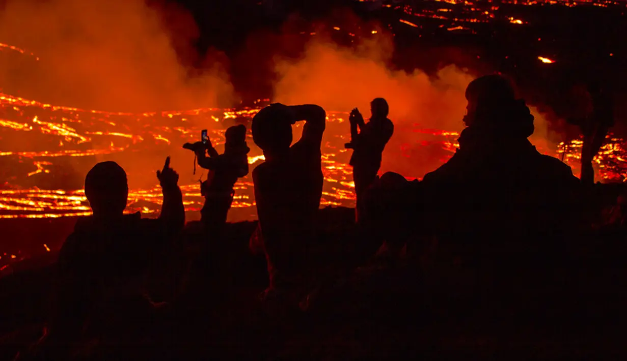 Orang-orang menyaksikan aliran lahar dari letusan gunung berapi di Semenanjung Reykjanes, barat daya Islandia, Senin (29/3/2021). Letusan gunung berapi tersebut tidak dipandang sebagai ancaman bagi kota-kota sekitar dan warga yang menyaksikan dari dekat. (AP Photo/Marco Di Marco)