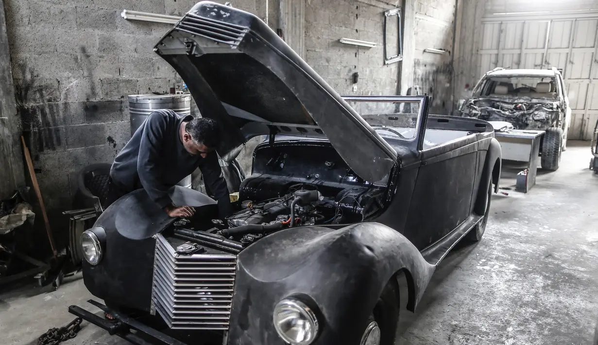 Munir Shindy mengecek mesin mobil tua di bengkelnya di Kota Gaza (28/10/2019).  Merestorasi mobil tua merupakan kegemarannya, namun sekarang Shindy kesulitan mendapat suku cadang yang dia butuhkan. (AFP Photo/Mahmud Hams)