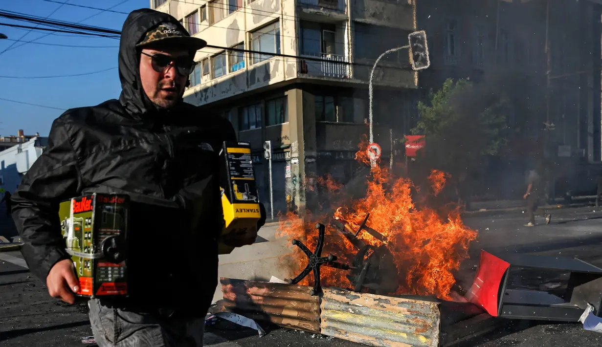 Seorang penjarah berlari melewati api unggun selama protes di Valparaiso, Chile, Minggu (20/10/2019). Bentrokan pecah di Santiago setelah dua orang tewas ketika sebuah supermarket dibakar ketika protes terhadap kondisi ekonomi dan ketidaksetaraan sosial. (JAVIER TORRES/AFP)