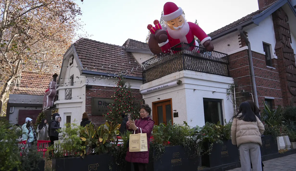 Orang-orang memotret dekorasi Sinterklas yang dipajang di sebuah bar dan bistro di Shanghai pada 17 Desember 2023. (AP Photo/Wayne Zhang)
