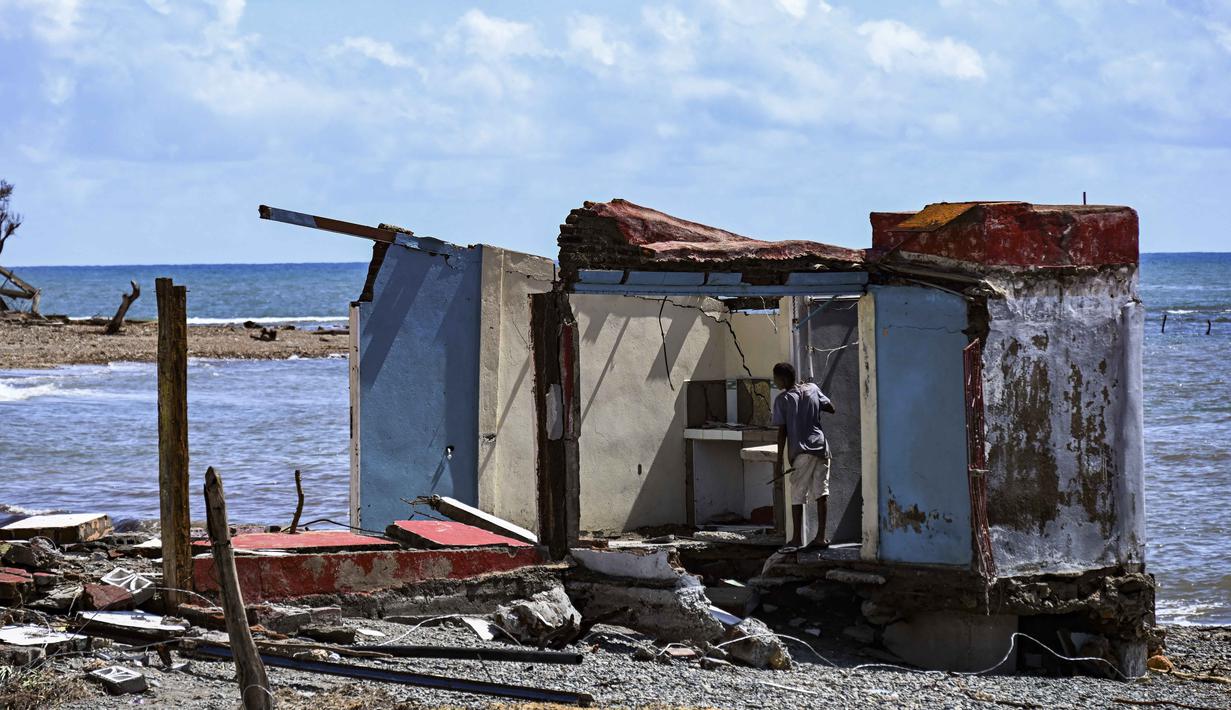 Seorang pria berdiri di samping sebuah rumah yang rusak akibat Badai Melissa di desa Boca de Dos Rios, provinsi Santiago de Cuba, Kuba pada Kamis 30 Oktober 2025. Sementara, kerusakan terparah dilaporkan terkonsentrasi di wilayah barat daya dan barat laut. (YAMIL LAGE/AFP)