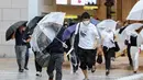 Pejalan kaki mencoba berlindung dari angin dan hujan saat mereka menyeberang jalan di depan Stasiun Osaka pada 15 Agustus 2023. (AFP/Jiji Press)