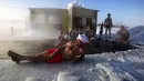 Seorang pria berbaring di atas es sementara anggota klub renang es berenang di dalam air es saat suhu turun hingga minus 34 derajat celcius, di Novosibirsk, Rusia, Sabtu (26/12/2020). Konon, tradisi semacam ini mereka lakukan karena diyakini baik untuk kesehatan. (Rostislav NETISOV/AFP)