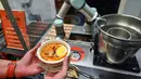 Seseorang memegang semangkuk laksa yang disajikan robot koki bernama Sophie di Singapura pada 26 Juli 2019. Pihak perusahaan menjamin, tidak ada rasa yang berbeda dari laksa buatan robot Sophie maupun buatan koki pada umumnya. (Roslan RAHMAN / AFP)