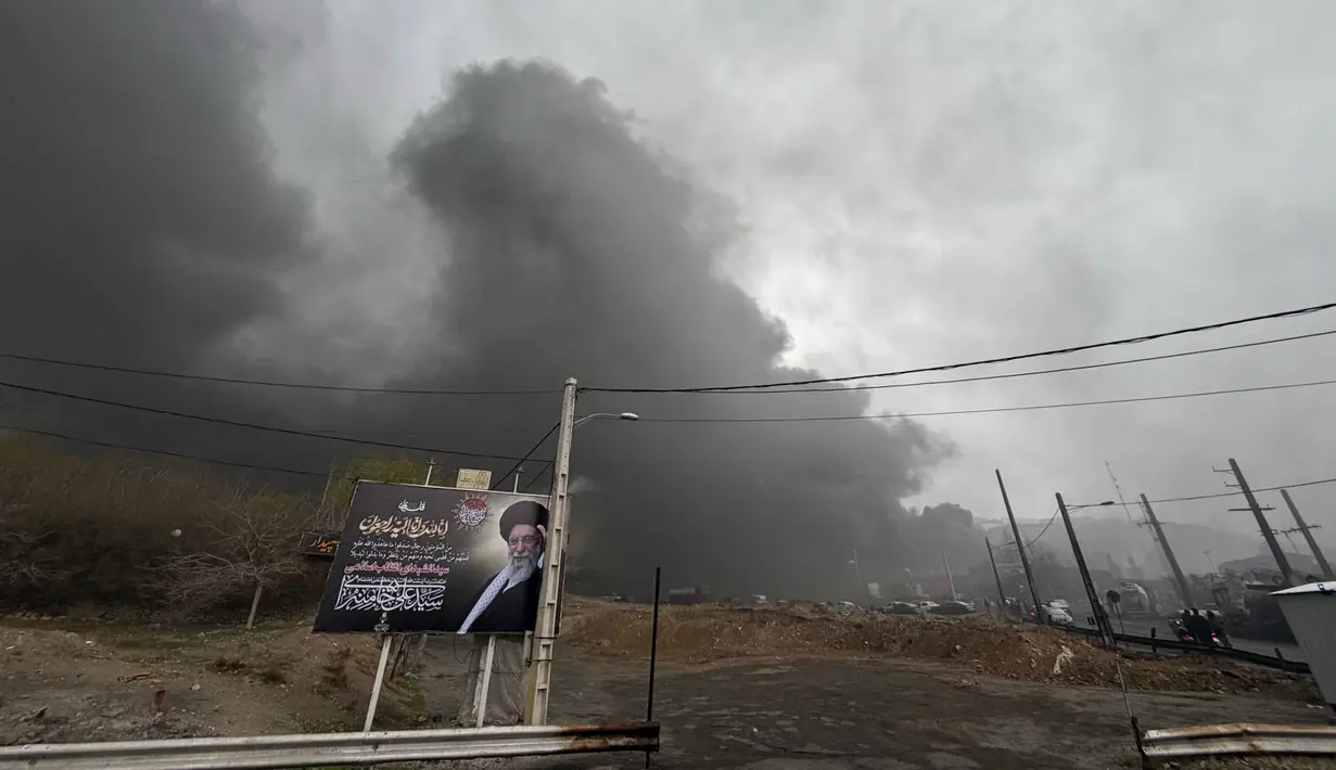 Kementerian perminyakan Iran menyatakan, salah satu depot minyak di Karaj, bagian barat Teheran, juga terkena serangan pada Sabtu 7 Maret 2026 malam. Tampak dalam foto, kepulan asap tebal dari serangan gabungan AS-Israel terhadap fasilitas minyak pada pada Sabtu 7 Maret 2026 malam masih terlihat di langit berawan di belakang papan reklame yang menampilkan mendiang Pemimpin Tertinggi Iran Ali Khamenei di Teheran, Minggu, 8 Maret 2026. (AP Photo/Vahid Salemi)