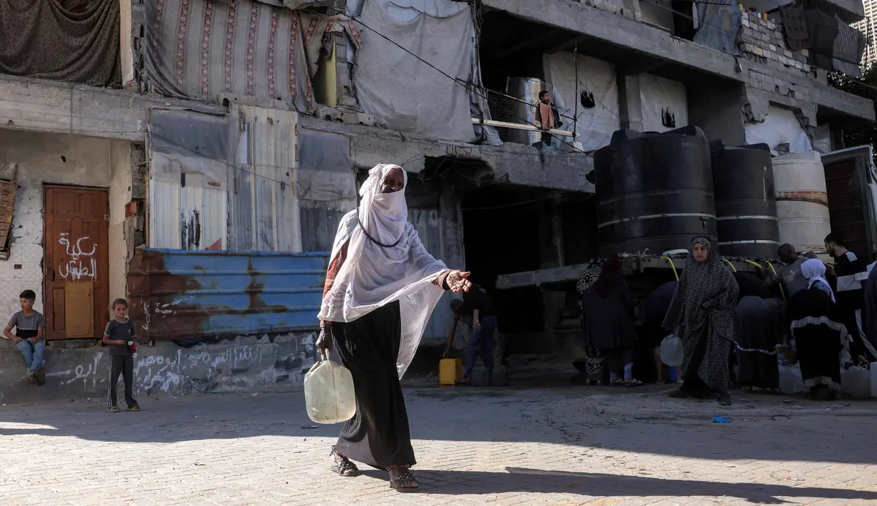 Seorang wanita berjalan dengan wadah air setelah mengisi tangki air di kamp penampungan, Khan Yunis, Jalur Gaza Selatan pada 6 Juni 2026. (Bashar Taleb/AFP)