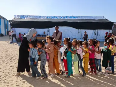 Guru-guru Palestina membariskan murid-murid di halaman sekolah yang didirikan oleh Asosiasi Kebudayaan Mayasem dengan dukungan UNICEF, sebelum pelajaran di kamp pengungsian di kawasan al-Qarara, Khan Yunis, di bagian selatan Jalur Gaza pada Selasa 7 Oktober 2025. (Omar AL-QATTAA/AFP)