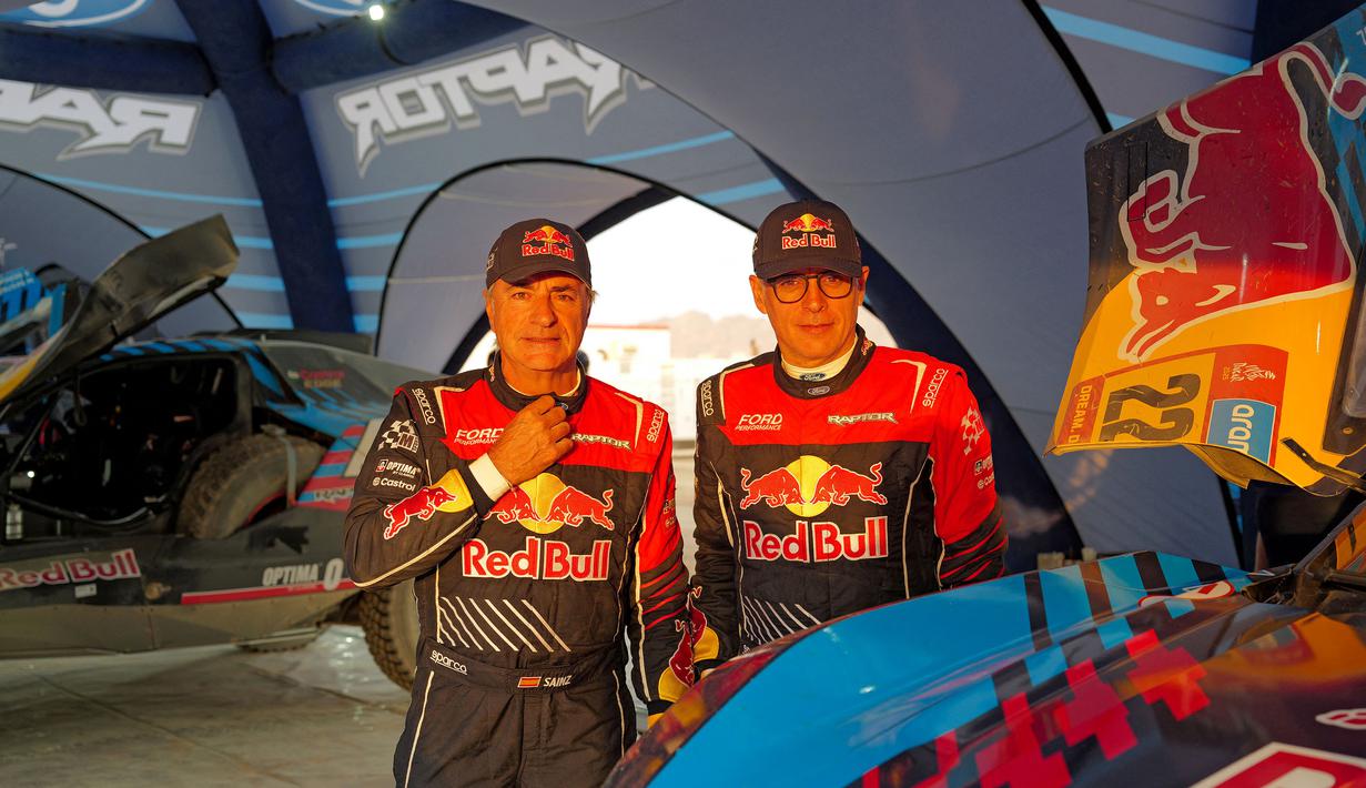 Pembalap Ford M-Sport, Carlos Sainz (kiri) dan co-driver Lucas Cruz tengah mempersiapkan mobilnya pada Rabu (01/01/2025) waktu setempat di Bisha, Arab Saudi. Ajang tersebut akan berlangsung pada 3 hingga 17 Januari 2025. (AFP/Valery Hache)