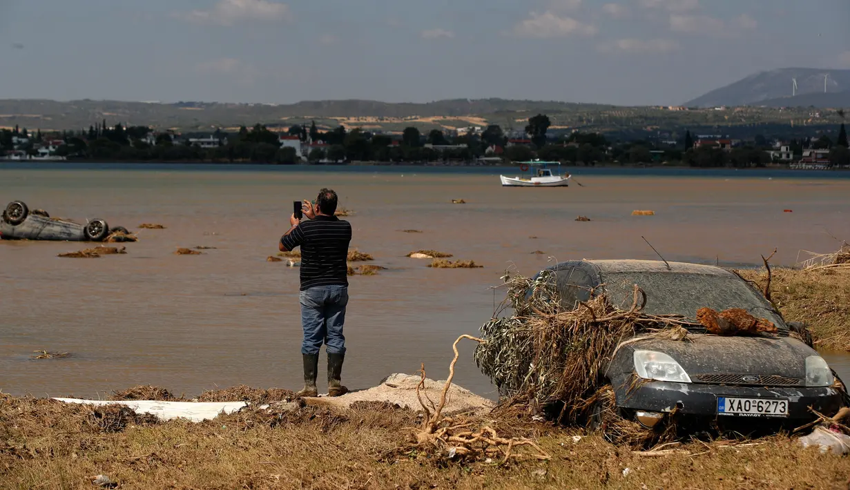 Penduduk lokal Christos Pavlou mengambil gambar mobilnya yang tenggelam setelah badai di desa Bourtzi di pulau Evia, Yunani, Senin (10/8/2020). Tujuh orang, termasuk dua lansia dan bayi berusia delapan bulan, tewas saat badai melanda pulau Evia pada Minggu kemarin. (AP Photo/Thanassis Stavrakis)