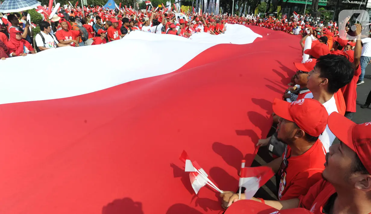 Relawan Jokowi-Ma'ruf Amin membawa bendera raksasa sepanjang sekitar 200 meter saat menyambut pelantikan Presiden-Wapres terpilih periode 2019-2024 di sekitar Patung Kuda, Jakarta, Minggu (20/10/2019). (merdeka.com/Arie Basuki)