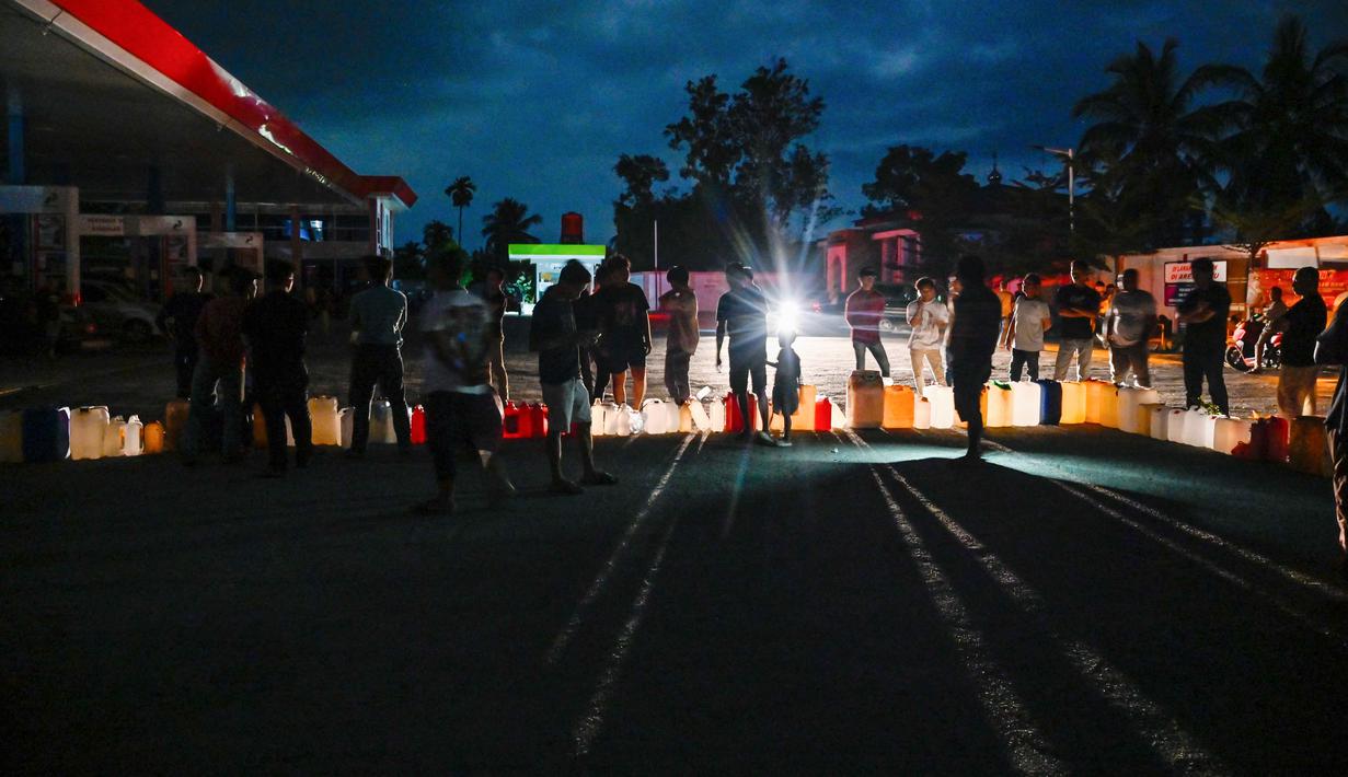 Beberapa SPBU bahkan terpaksa menutup operasional karena tidak memiliki jenis BBM yang memadai untuk dijual kepada masyarakat. Tampak dalam foto, warga terdampak banjir mengantre untuk mendapatkan bahan bakar di sebuah Stasiun Pengisian Bahan Bakar Umum (SPBU) di Samahani, Provinsi Aceh, pada 2 Desember 2025. (CHAIDEER MAHYUDDIN/AFP)