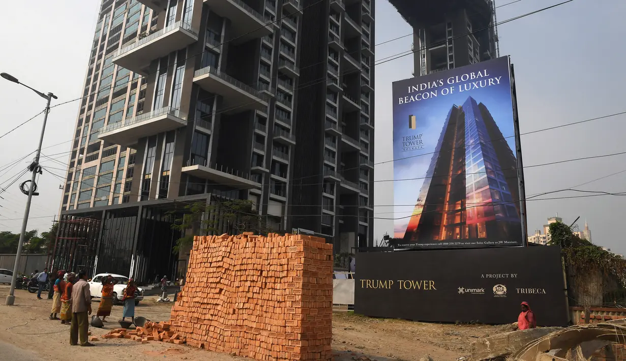 Sejumlah buruh wanita India berdiri di depan papan iklan Trump Tower di Kolkata, India (20/2). Putra tertua Presiden Amerika Serikat Donald Trump yakni Donald Trump Jr. dijadwalkan tiba di India pada selasa (20/2). (AFP/ Dibyangshu Sarkar)