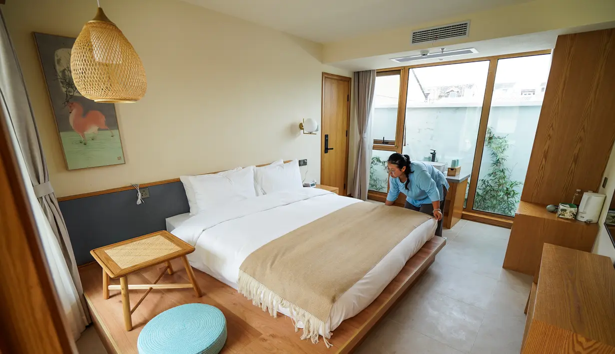 Seorang staf merapikan tempat tidur di Hotel Gusu Yard di Suzhou, Provinsi Jiangsu, China Timur (29/7/2020). Hotel Gusu Yard, sebagai nama penginapan berkualitas tinggi, telah mendirikan empat cabang di kota tersebut dan berencana membangun lebih dari 80 cabang baru di masa mendatang. (Xinhua/Li Bo)