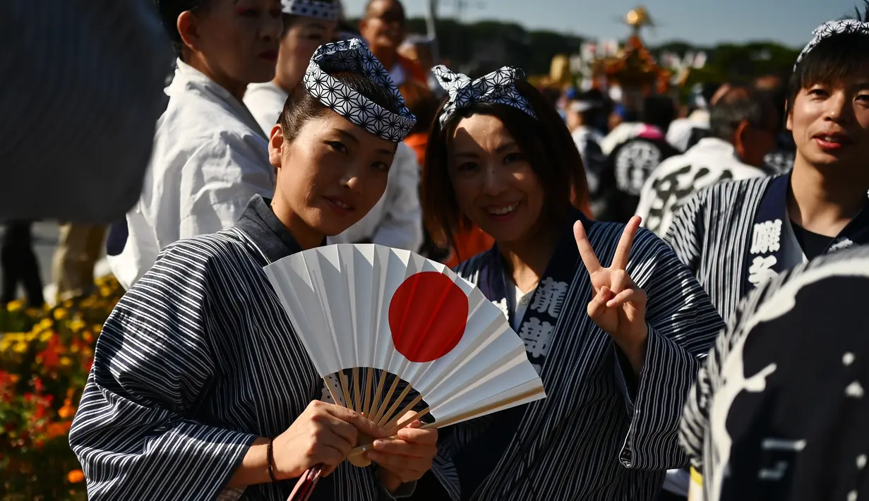 Dua wanita berpose saat mengikuti perayaan nasional untuk menandai penobatan Kaisar Jepang Naruhito di depan Istana Kekaisaran di Tokyo (9/11/2019). Kaisar Naruhito menjalankan ritual penobatannya setelah dilantik pada 1 Mei 2019. (AFP Photo/Charly Triballeau)