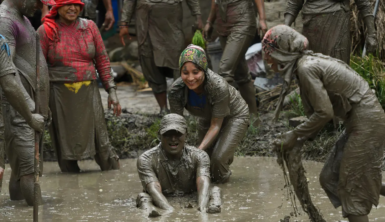 Para petani berlumur lumpur saat bermain pada Hari Padi Nasional di sawah Desa Tokha, Kathmandu, Nepal, Senin (29/6/2020). Para petani di Nepal merayakan Hari Padi Nasional sebagai musim tanam padi tahunan dimulai. (PRAKASH MATHEMA/AFP)