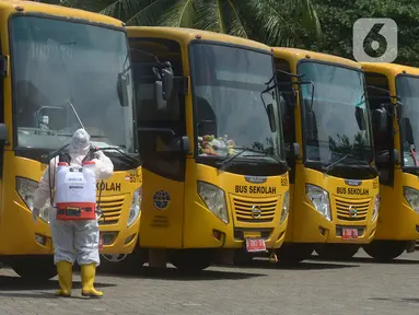 Petugas ber-APD menyemprotkan disinfektan pada bus sekolah di Posko Gabungan PSBB dan Gakplin Protkes, Puskesmas Jatinegara, Jakarta, (22/9/2020). Sejumlah unit bus sekolah kini dialihfungsikan menjadi kendaraan untuk mengantar pasien Covid-19 berstatus OTG menuju Wisma Atlet. (merdeka.com/Imam Buho