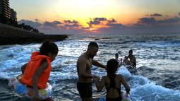 Seorang pria bersama dua putrinya berenang di Laut Mediterania dari Corniche, atau promenade tepi laut, saat matahari terbenam pada hari terakhir musim panas, di Beirut, Lebanon (20/9). (AP Photo / Hussein Malla)
