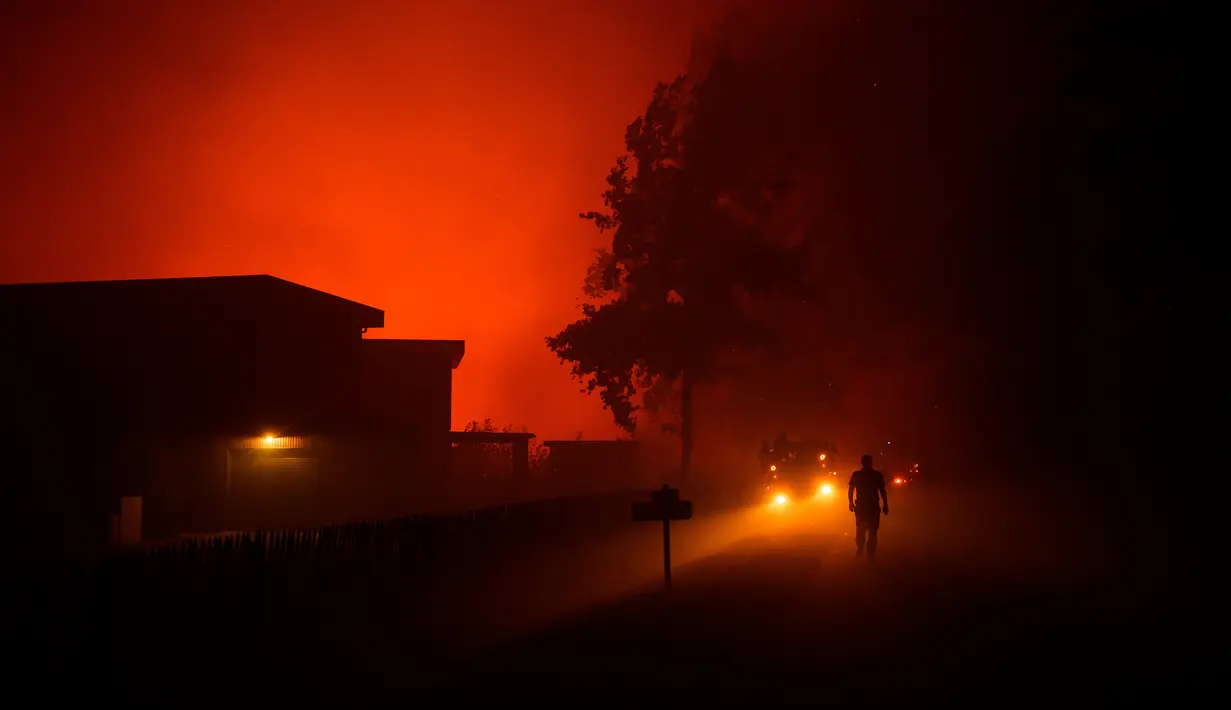 Seorang petugas pemadam kebakaran berjalan melewati rumah-rumah yang terancam oleh kebakaran hutan di Saumos dekat Bordeaux, Prancis barat daya (12/9/2022). Kebakaran yang berlangsung sejak 12 September 2022 telah menyebar sekitar 1800 hektar vegetasi dan hutan di Saumos dan memaksa evakuasi kota dalam konteks suhu tinggi di Gironde. (AFP/Philippe Lopez)