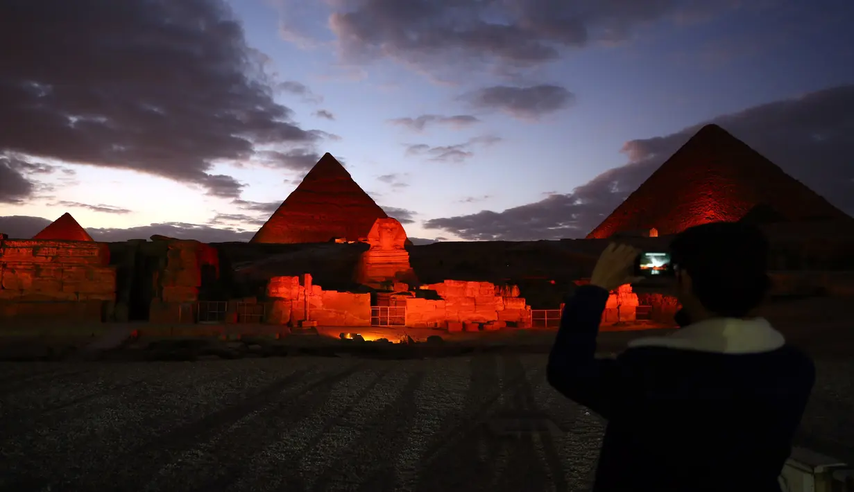 Seorang pria mengambil gambar patung Sphinx dan sejumlah piramida yang berwarna merah saat pertunjukan cahaya dan suara di Giza, Mesir, Kamis (23/1/2020). Pertunjukan tersebut digelar sebagai bagian dari perayaan Tahun Baru Imlek. (Xinhua/Ahmed Gomaa)