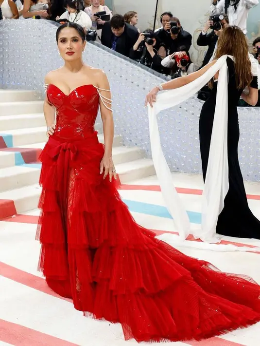 Salma Hayek tampil seperti emoji dengan gaun merah Gucci-nya yang berani. Begitu juga riasan dari Sofia Tilbury dengan bibir merah yang bold. [@themetgalaofficial]