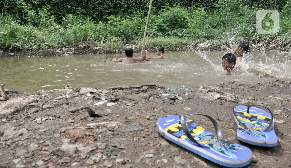 Anak-anak berenang di kubangan air di depan Apartemen Green Pramuka, Jakarta, Rabu (5/2/2020). Keterbatasan ekonomi dan minimnya lahan bermain membuat sekelompok anak sekolah dasar ini memilih berenang di kubangan meskipun mereka tahu air kotor dapat menimbulkan penyakit. (merdeka.com/Iqbal Nugroho)