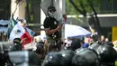 Pengunjuk rasa juga membawa simbol bendera bajak laut "One Piece". Tampak dalam foto, seorang pengunjuk rasa bertopeng tengkorak melihat ke arah polisi anti huru hara dalam demonstrasi Generasi Z melawan pemerintahan Presiden Meksiko Claudia Sheinbaum, di sepanjang Reforma Avenue di Mexico City, pada 20 November 2025. (Yuri CORTEZ/AFP)