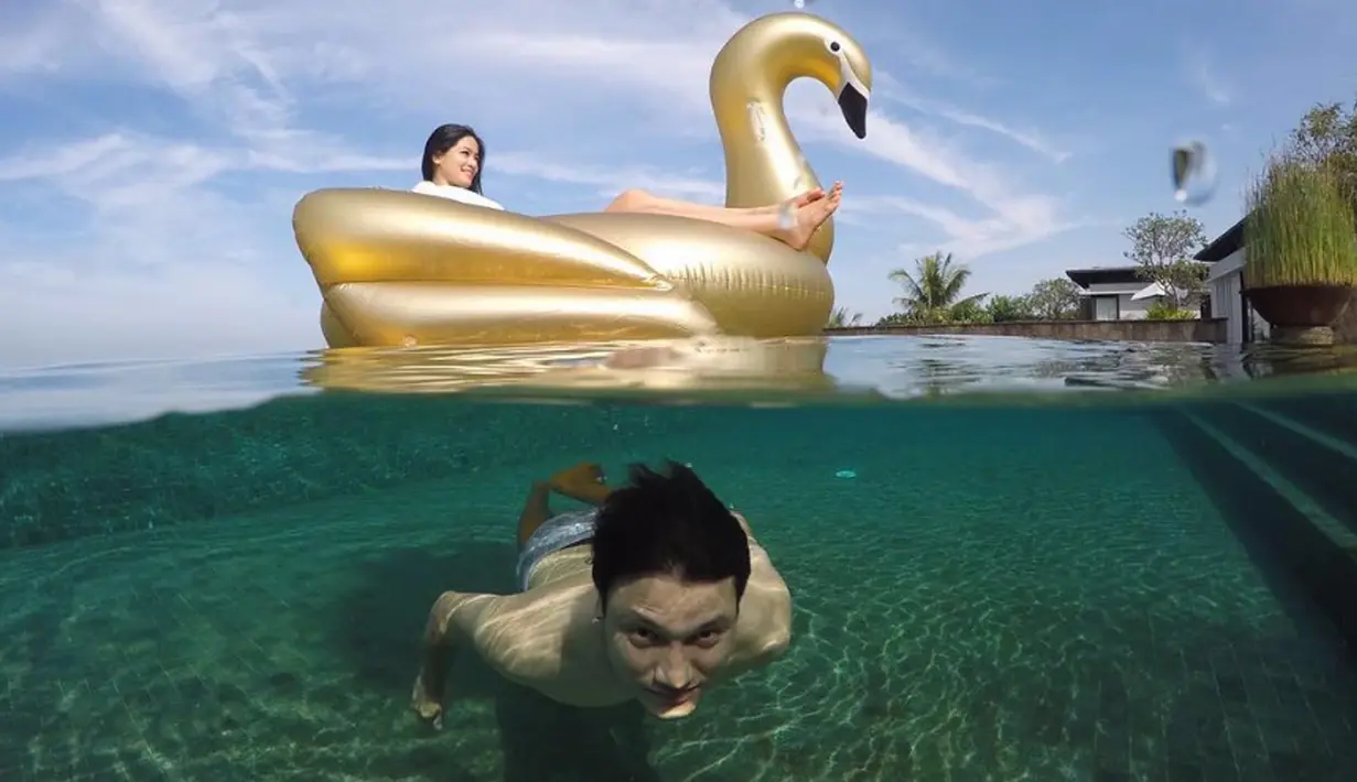 Christian Sugiono berenang di dalam air sementara Titi Kamal asyik berada di atas pelampung berbentuk bebek. Foto ini diambil saat Titi dan keluarga kecilnya mengisi liburan di Bali. (instagram.com/titi_kamall)