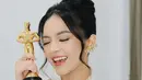 Sambil memegang piala kemenangan, Eca Aura memilih mengenakan kebaya putih dengan aksen bordiran bunga ditambah bordiran warna bunga biru di bagian bawah. Dipadukan inner putihnya.  [elsaajapasal]
