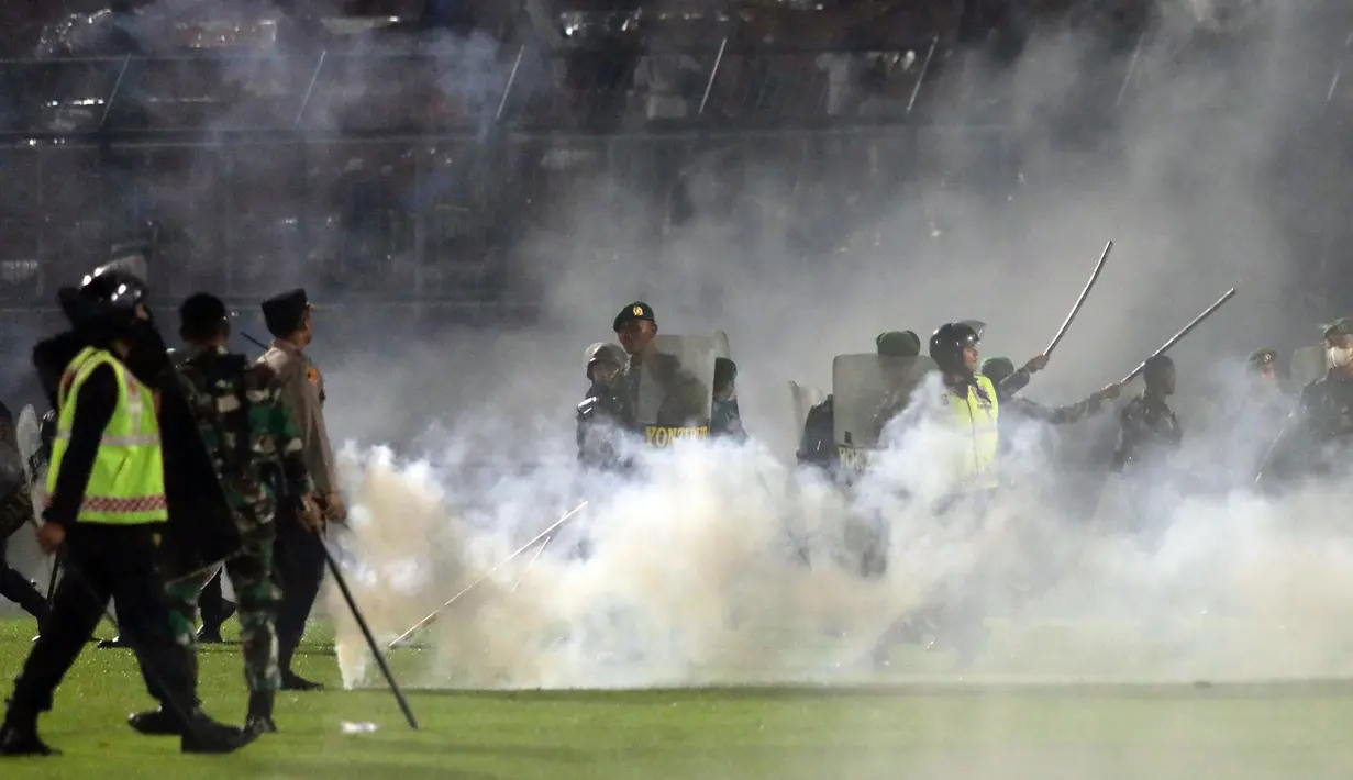 Polisi dan tentara berdiri di tengah asap gas air mata saat kerusuhan pada pertandingan sepak bola antara Arema Vs Persebaya di Stadion Kanjuruhan, Malang, Jawa Timur, 1 Oktober 2022. Ratusan orang dilaporkan meninggal dunia dalam tragedi kerusuhan tersebut. (AP Photo/Yudha Prabowo)