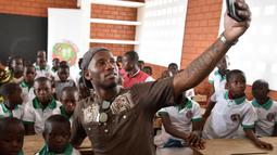 Didier Drogba melakukan foto selfie bersama anak-anak saat membuka sekolah dasar di Onahio, Pokou-Kouamekro, Pantai Gading, (20/1/2018).  Drogba menjadi salah satu sponsor utama untuk sekolah tersebut. (AFP/Sia Kambou)