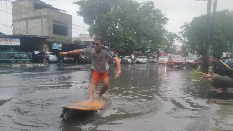 Warga berselancar saat banjir di Medan.