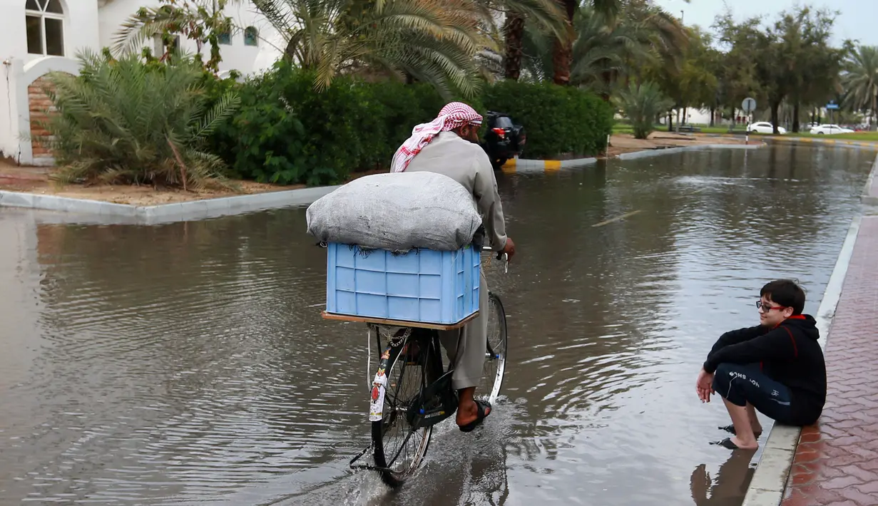 Seorang pria mengendarai sepeda di jalan banjir usai badai hujan, Abu Dhabi (9/3/2016 ). Akibat hujan lebat ini, sekolah diliburkan dan penerbangan ditunda. (AFP Photo)