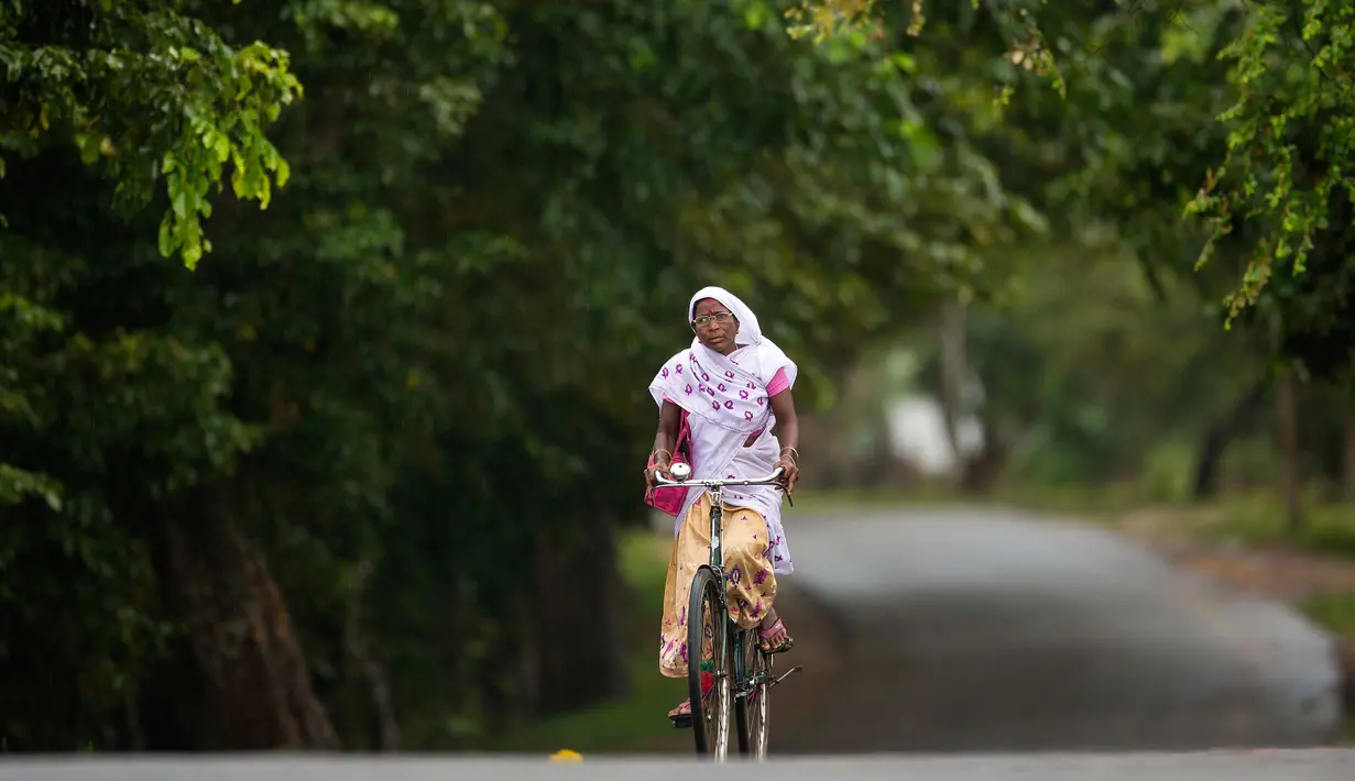 Seorang wanita asal Assam mengenakan pakaian tradisional mengendarai sepeda di Kaziranga, India, (11/10). Daerah ini terkenal dengan Taman Nasional Kaziranga. (AP Photo/Anupam Nath)