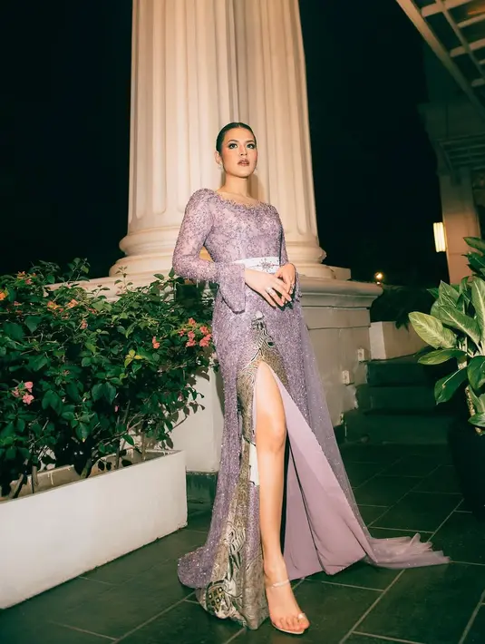 Kebaya berwarna ungu keabuan ini dihiasi dengan detail payet berkilauan yang membalut tubuhnya dengan sempurna, menciptakan efek glamor yang tetap terasa lembut. Potongan lengan panjang dengan aksen ruffle di pergelangan menambah kesan dramatis, sementara belt berwarna perak dengan detail ornamen memberi sentuhan klasik yang semakin memperindah siluetnya.  [@raisa6690].