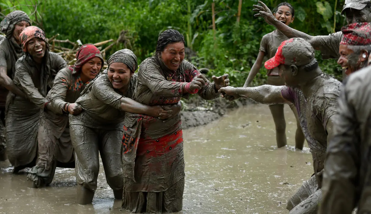 Para petani berlumur lumpur saat bermain pada Hari Padi Nasional di sawah Desa Tokha, Kathmandu, Nepal, Senin (29/6/2020). Para petani di Nepal merayakan Hari Padi Nasional sebagai musim tanam padi tahunan dimulai. (PRAKASH MATHEMA/AFP)